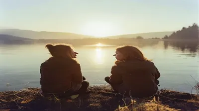 Two friends in quiet conversation by lake.
