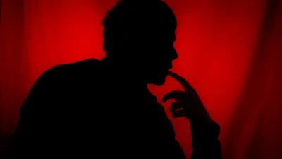 A moody silhouette of a person deep in thought against a striking red background.