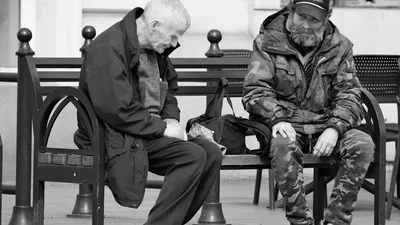 Two men share a moment on a city bench, captured in monochrome.