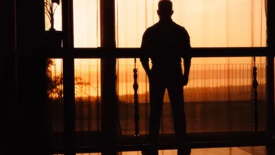 A silhouette of a man standing by a window at sunset, creating a dramatic and reflective mood.