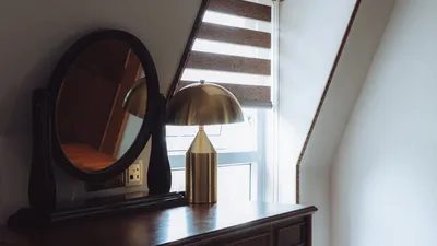 Elegant interior scene featuring a vintage mirror and brass lamp on a wooden table by a window.