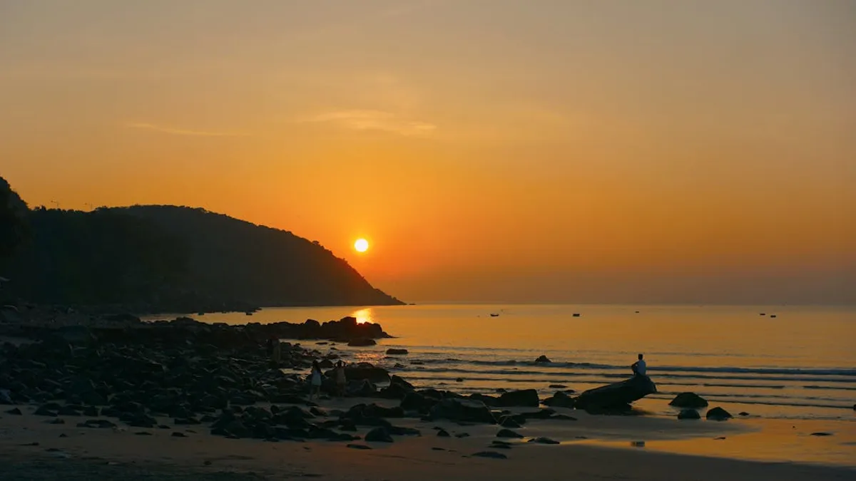 Peaceful beachside sunset scene with silhouette of person and rocky shore.