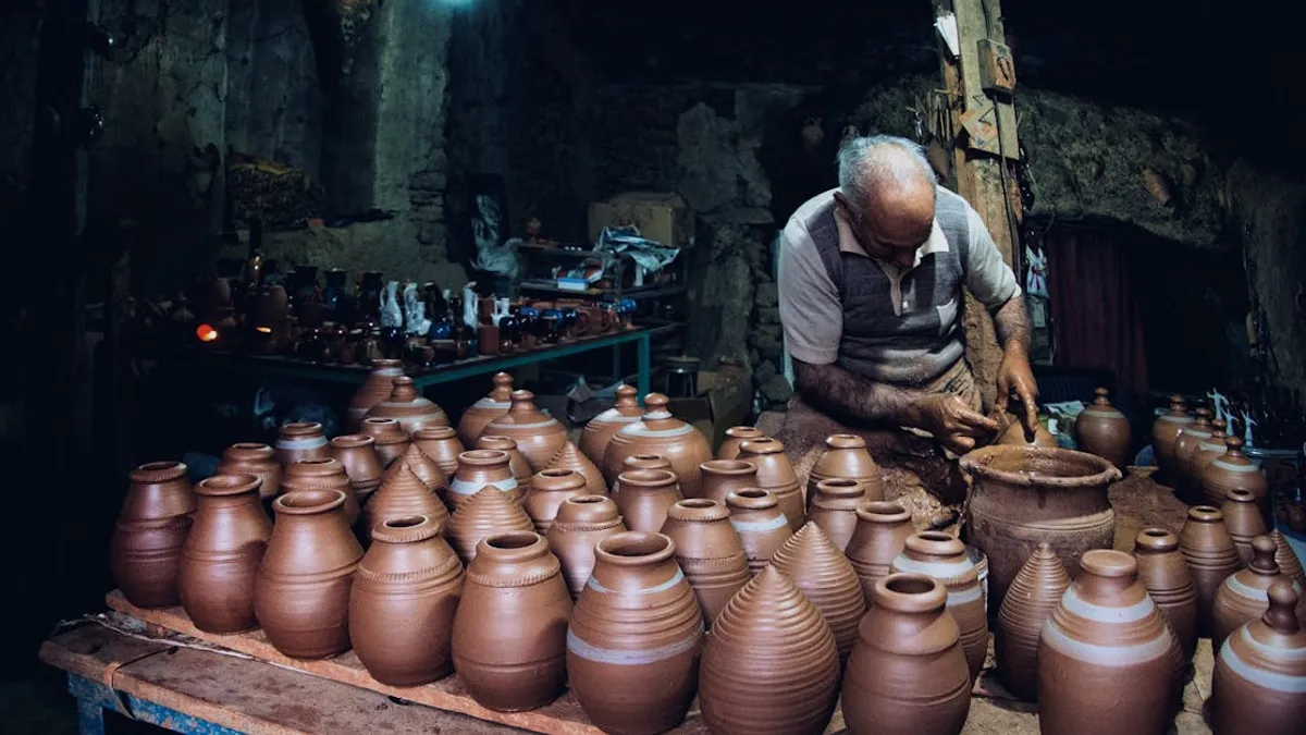 Elderly potter skillfully shapes clay in a dimly lit workshop surrounded by handcrafted pots.