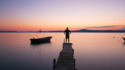 Lonely figure on a wooden pier overlooking calm water during a colorful sunset.