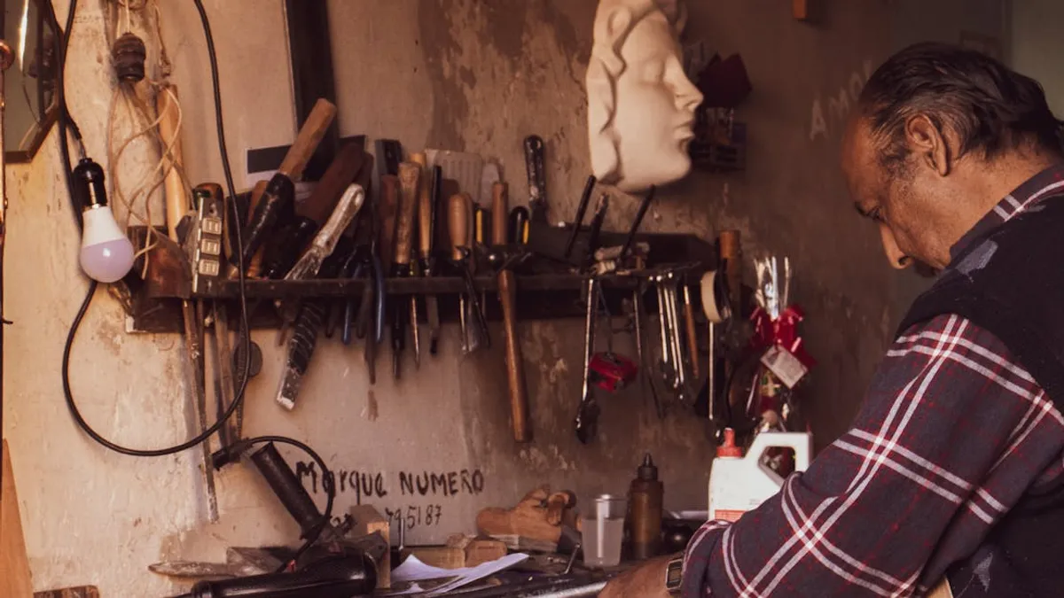 Craftsman focused on work in vintage workshop with tools and sculptures.