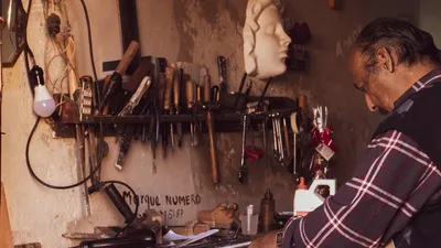 Craftsman focused on work in vintage workshop with tools and sculptures.