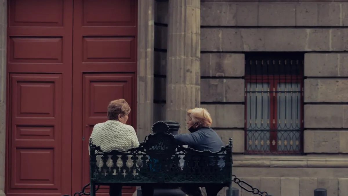 Two senior women sitting and talking on a decorative bench outside a building.