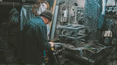 A blacksmith in a workshop shaping metal with various tools and equipment around.