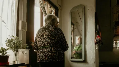 Elderly woman gazes at her reflection in a warm, cozy home setting with decor.