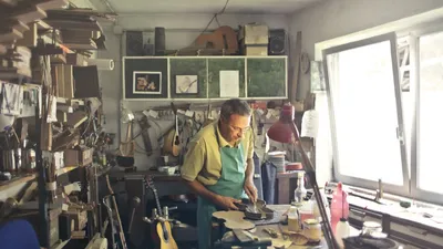 A dedicated craftsman working on musical instruments in a sunlit workshop.